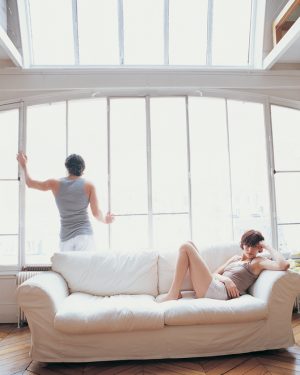 One partner sits on sofa, upset, while other partner, turns away to window