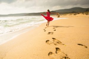 Rear view of person in red dress dancing in carefree way on the beach