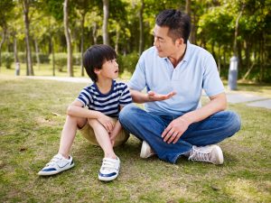 A father sits with child on the grass as the two talk seriously