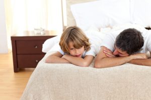 Father and adolescent child lie on bed, heads on their arms, having a conversation