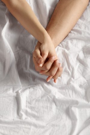 Close-up shot of forearm and hands of couple on white sheet