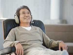 Mature man leans back in armchair, wearing headphones, smiling