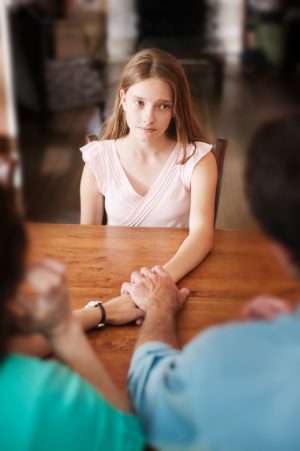 Cropped rear view of parents reaching across table to clasp hand of sad-looking teenager
