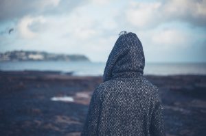 Person wearing hood looks out over shallow tide at beach