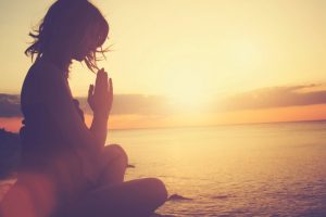 Sitting cross-legged in yoga pose on beach at sunset