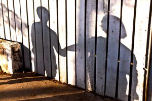 White painted fence displays shadow of teen boy taking adult's outstretched hand