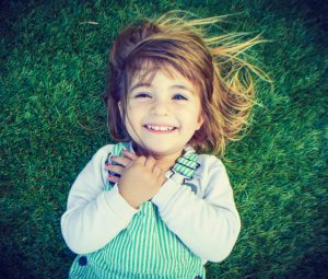 Overhead view of smiling child lying back on field of grass with hands over heart