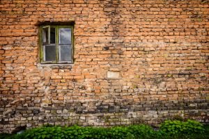 Old red brick wall with small window and green grass