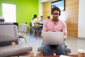 Person wearing headphones sits alone in open office, smiling while working on laptop