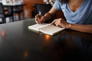 person writing thoughts in notepad diary