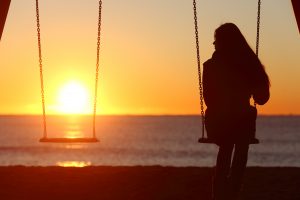 Girl looking at empty swing at sunset