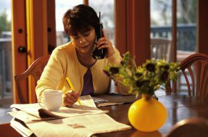 Person in yellow sweater sits at desk with papers and classified ads making phone calls