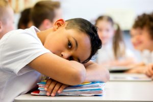 Close-up shot of child with head on books looking out at camera with blank expression