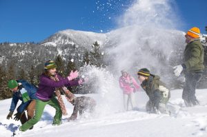 Large group of people of different ages throw snowballs by hills under blue sky