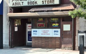 Storefront of adult bookshop with signs saying "OPEN" and "Largest Video Selection"
