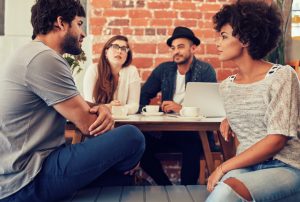 Group of millennials from different backgrounds sit and talk at coffee shop