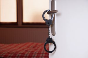 Handcuffs hanging from knob of bedroom door that stands open to show bed with plaid blanket