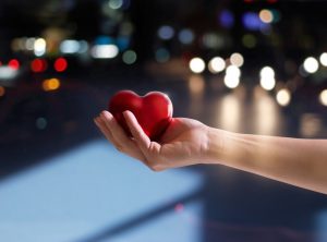 hand holding heart in front of city scene