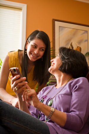 Seated, smiling mother holds up cell phone, daughter smiles and leans over to look