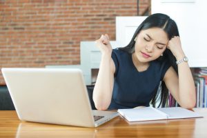 Young professional sits in front of laptop with open notebook, head on hand, looking bothered