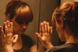 Person with downcast expression places hands on mirror 