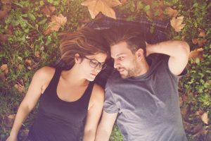 Upper-body view of couple with reserved expressions lying on grass scattered with autumn leaves
