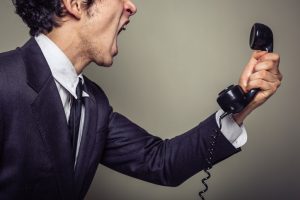 Upper body photo of person in business suit holding phone away from face and shouting into it