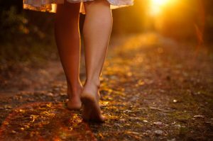 View of a person's legs walking towards the sunset on a dirt road