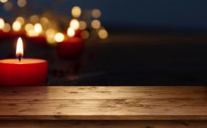 Single red candle burns on empty wooden table, blurred lights in dark background