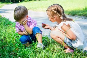 Child in white dress with braided hair offers flower to upset child with short hair