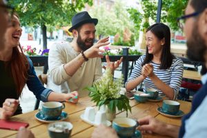 A group of friends sit at cafe table, talking and laughing happily