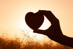 Hand holding heart against beautiful setting.