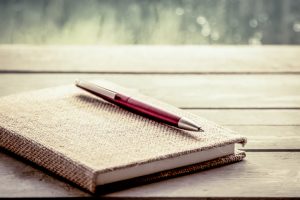 Pen lies on notebook on wooden table with rainy weather visible outside window