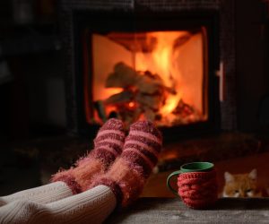 Legs in socks rest in front of fireplace in dark room, with a red and green mug nearby