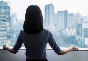 Rear view of a person with shoulder-length hair wearing business attire looking out the window at cityscape in Beijing, China