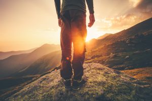 Lower half of a traveler standing on mountain at sunset looking over mountain valley