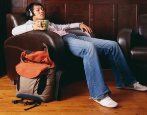 Young adult holds mug of tea and reclines in armchair wearing headphones