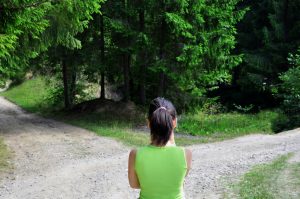 Person with ponytail stands looking down forked road, apparently trying to decide on a direction