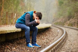 Fall scene of young adult with head in hands sits on ledge next to curving train track