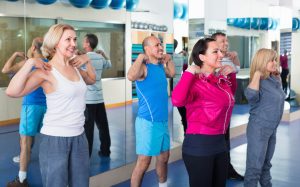 A group of people of different ages and sizes exercising in Pilates class while smiling