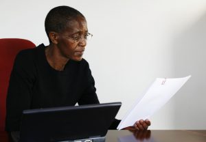 Person of color with shaved head and glasses sits at well-made desk and reviews legal papers