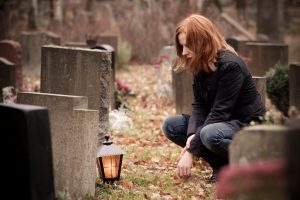 person crouching at grave stone