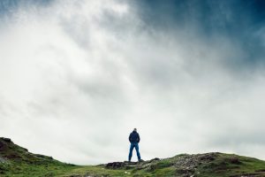 Distance rear view shot of single person looking over hilltop under stormy sky