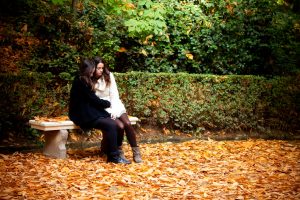 Two young people with long hair wearing coats and warm clothes sit on a bench in carpet of autumn leaves