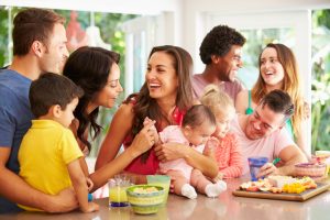 Several parents and children at table talk to each other while holding children