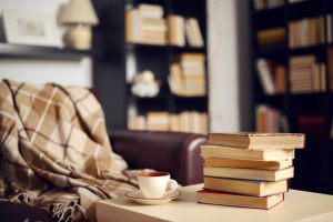 Focus is on corner with soft blanket, tea, and books. Two tall bookcases in blurred background
