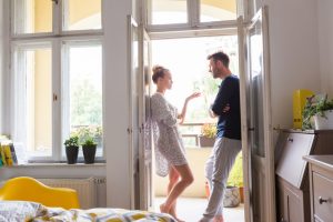 Couple standing in open doorway in front of open window at home in the morning.