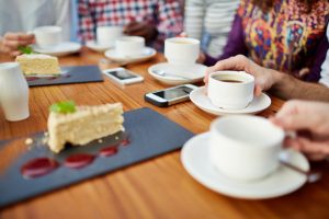 Focus on cake and tea at restaurant table, cropped view of several friends with smartphones on table
