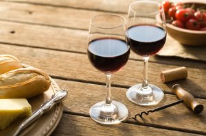 Two half-filled glasses of red wine on picnic table with bread and cheese in the afternoon