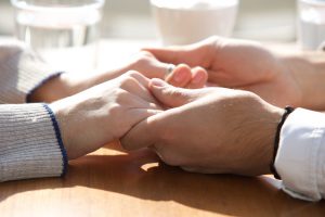 Close-up shot of two people holding hands on top of a table, water glasses out of focus in background